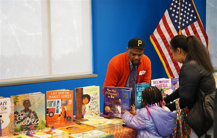 A woman and a child looks at books with a man behind assisting them.